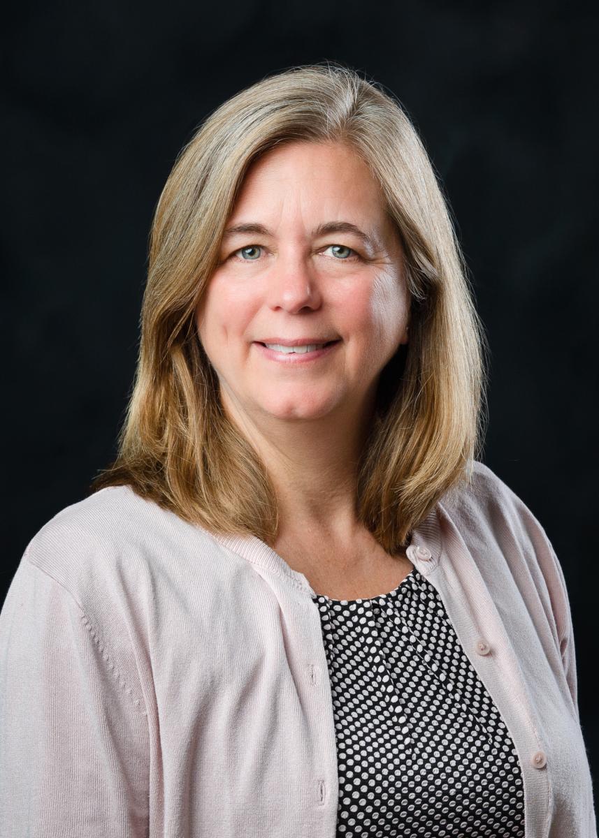 Headshot of Devon Brenner wearing a pink sweater with a black background.