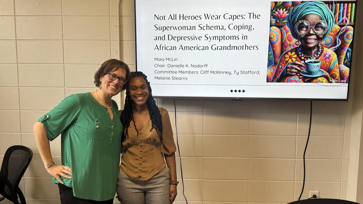 Dr. Danielle Nadorff and Maia McLin smile together in front of a screen showing the title slide of Maia's dissertation defense.